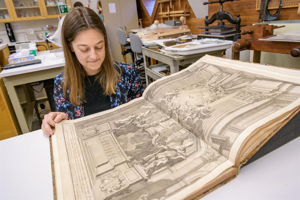 Laura McNulty, library and archival materials conservation major, (WUDPAC 2021), examines one of her treatment objects, a collection of prints by Piranesi  (Image credit Evan Krape, University of Delaware).